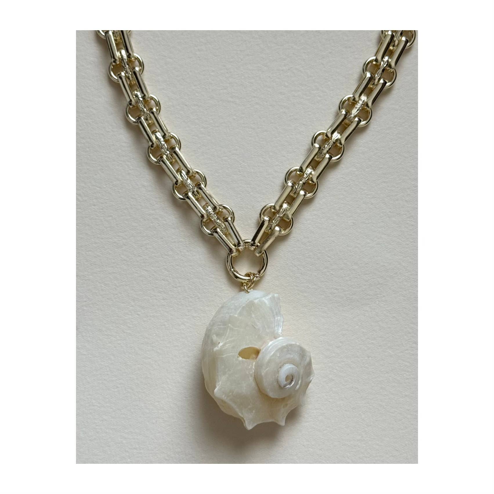 The Golden Nautilus Necklace by Tramps+Thieves features a gold-filled chain with large round links and a white spiral seashell pendant, creating an elegant coastal style. Photographed against a plain light background.