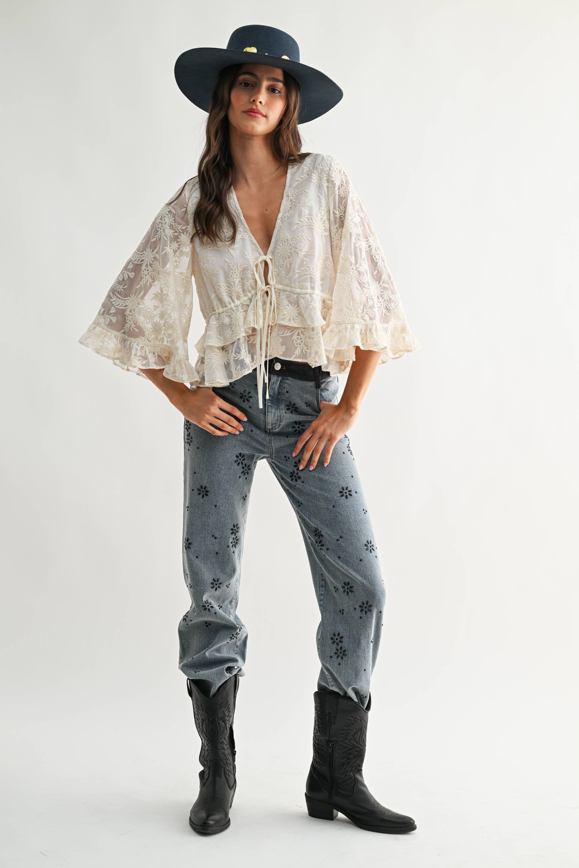 Woman wearing Boho Embroidered Sheer Blouse with wide sleeves, paired with patterned jeans, black boots, and a black hat