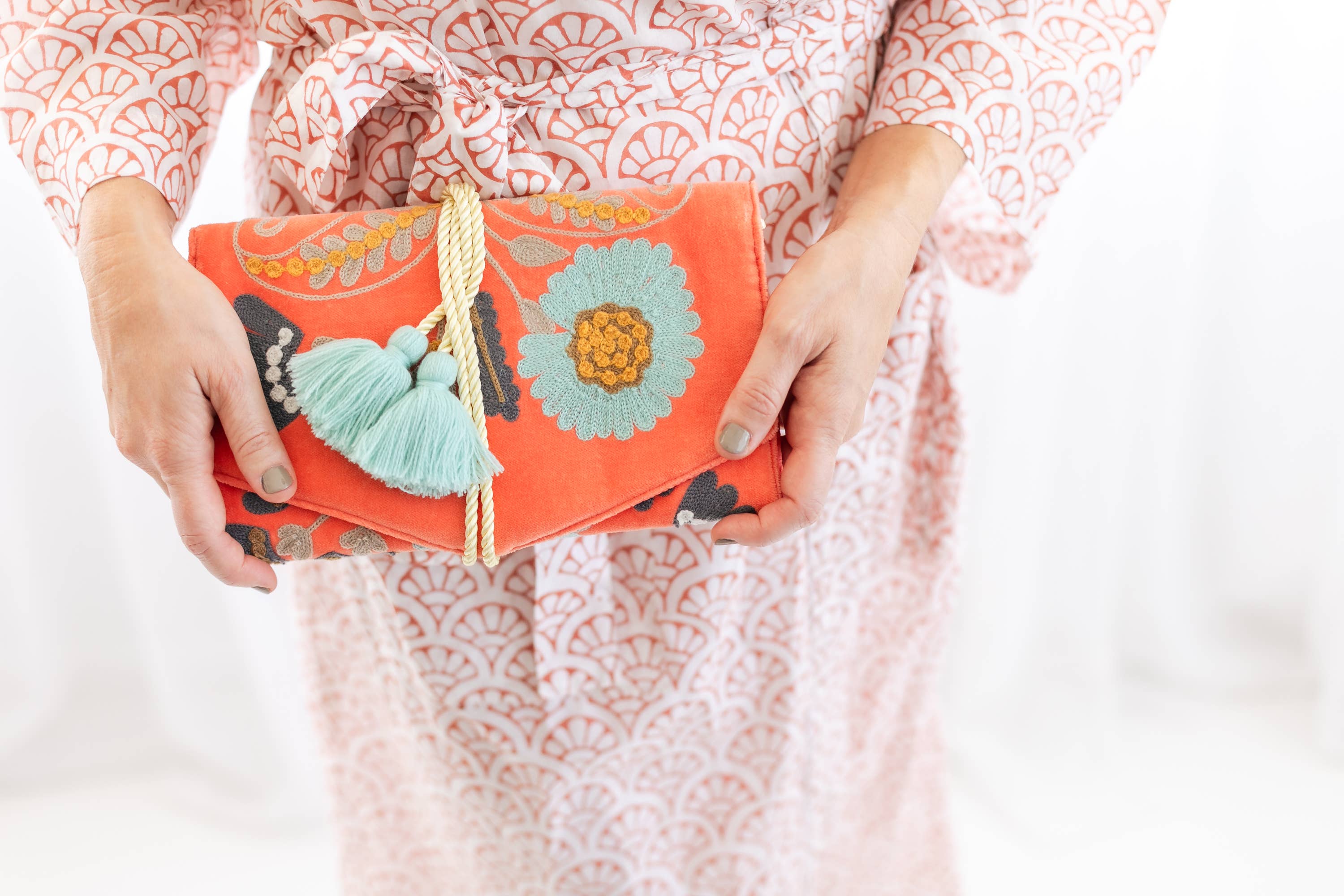 Person holding vibrant Embroidered Velvet Jewelry Organizer-Coral adorned with blue tassels and floral designs