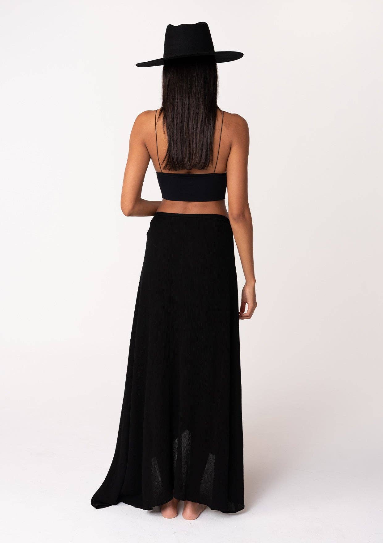 Woman wearing a black Summer Solid Wrap Maxi Skirt paired with a black top and wide-brim hat, viewed from behind