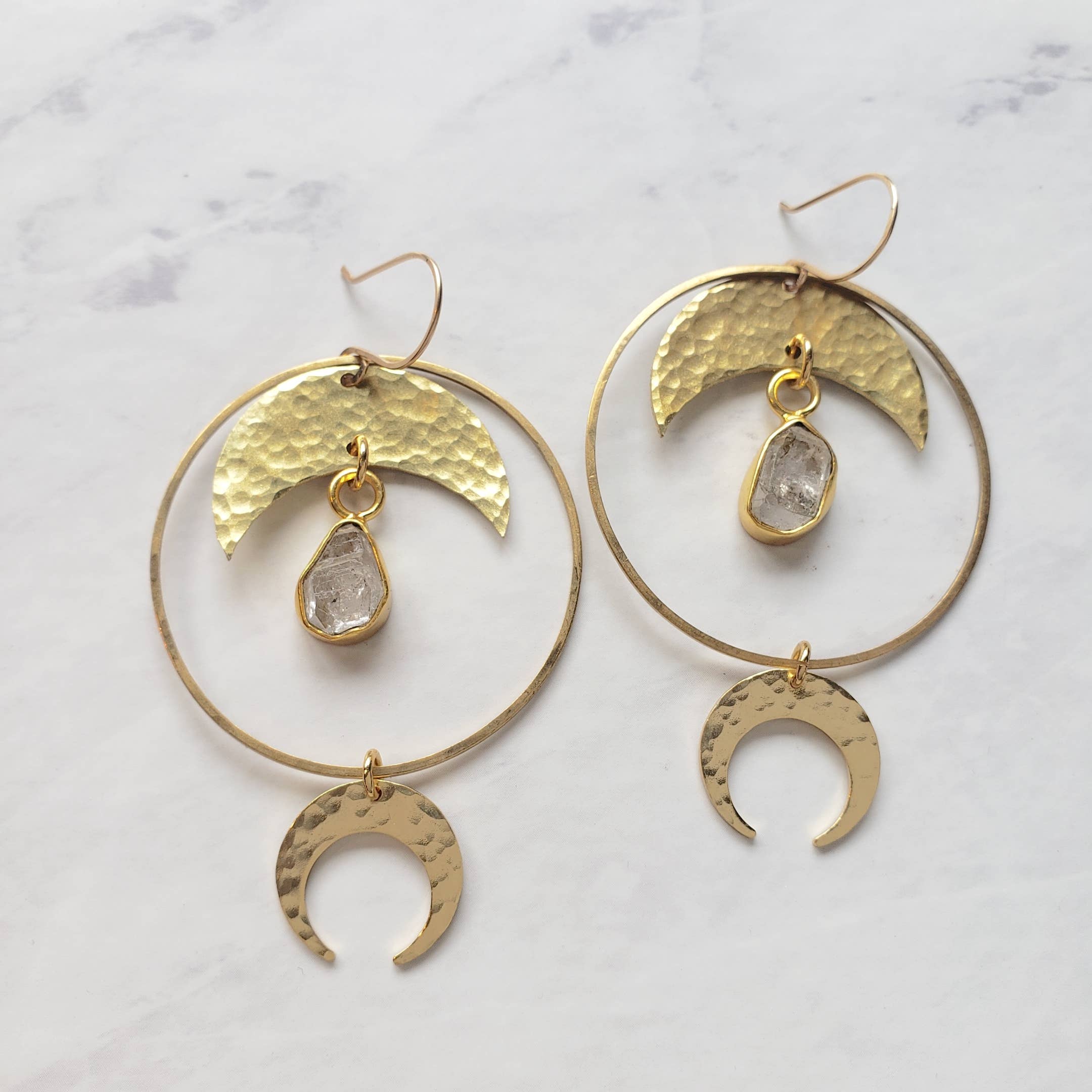 Quartz Halo Moon Hoops feature hammered gold crescent shapes and raw quartz stones in large circular earrings