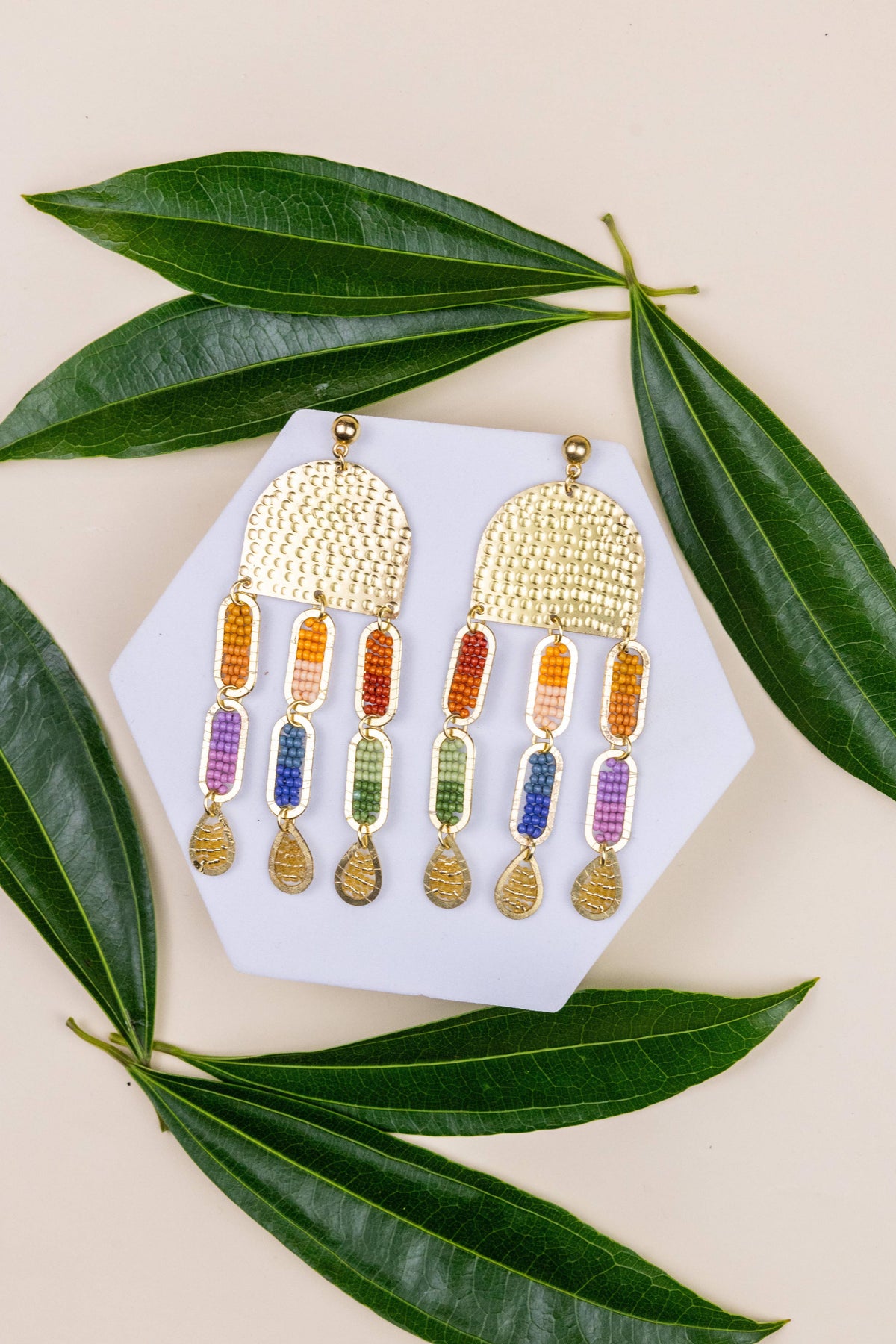 Iris Sun Earrings with colorful beaded drops displayed on a white card among green leaves