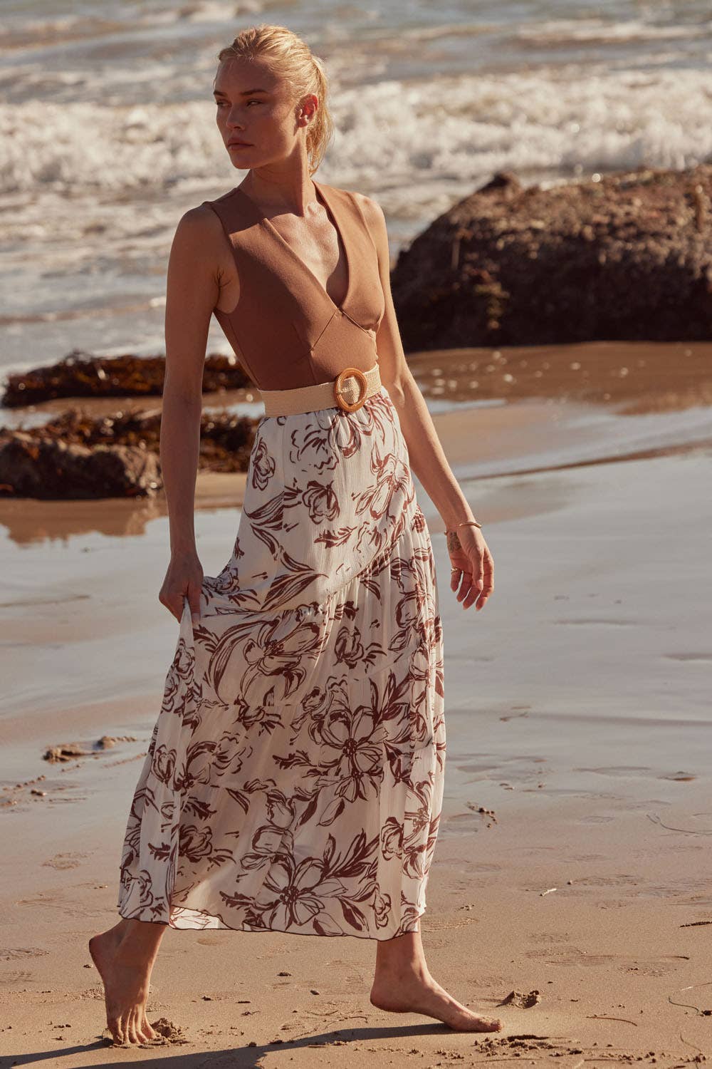 Woman walking barefoot on beach wearing Essential Trends Crepe V-Neck Bodysuit paired with floral maxi skirt and belt