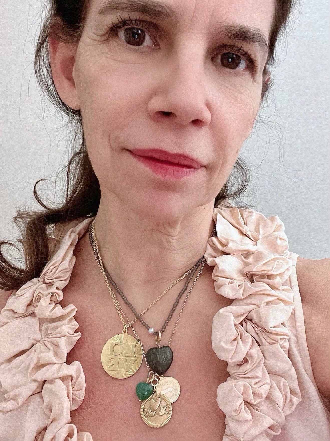 Close-up of woman wearing layered necklaces featuring a gold LOVE pendant with textured chains and stones