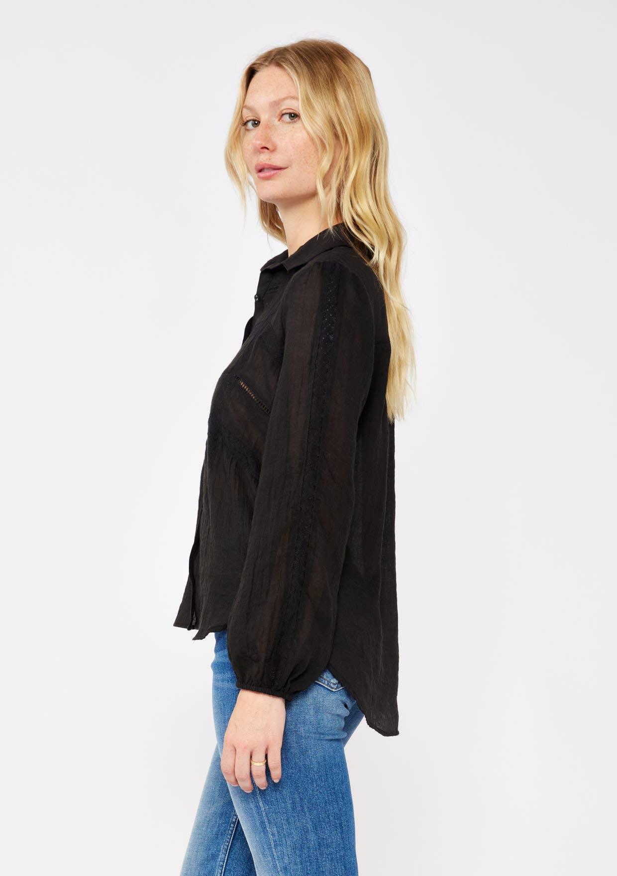 Woman wearing black Crinkled Lace Long Sleeve Button Down Blouse paired with blue jeans in a side pose