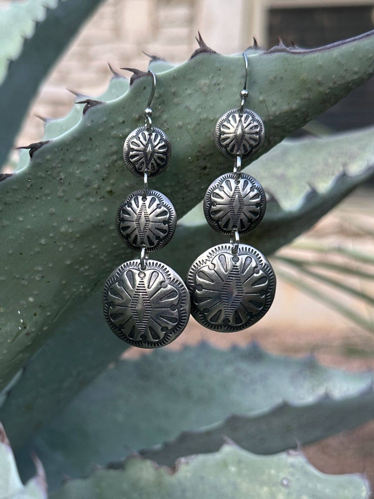 17885 Graduated Triple Concho Earring displayed on plant, featuring detailed artisan metalwork for bold statement style