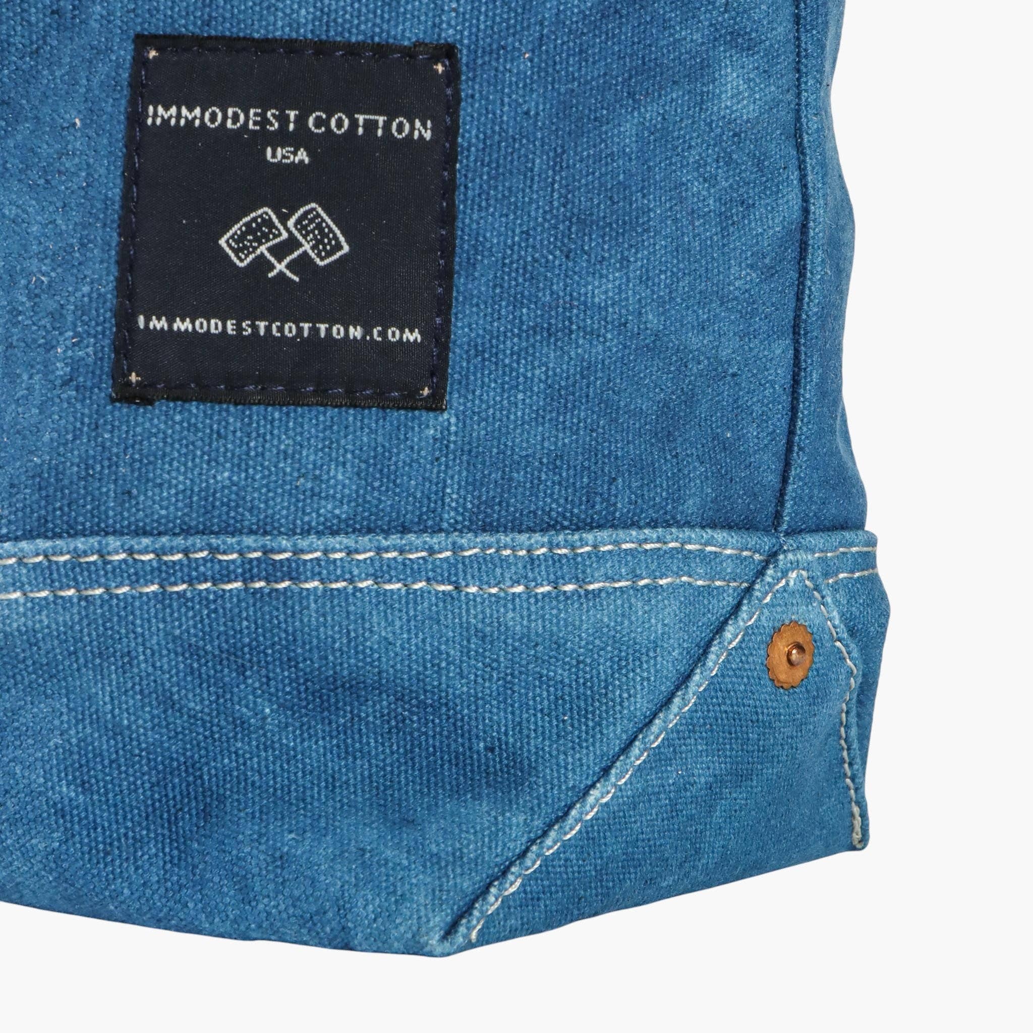 Close-up of blue denim fabric with a 'Immodest Cotton' label on a white background