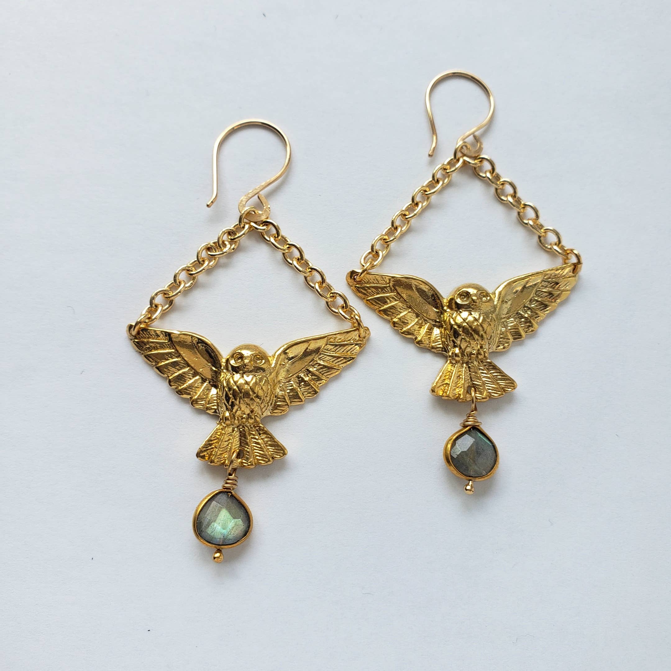 Dreamers of Dreams Gold Owl Labradorite Charm Dangle Earrings feature intricately detailed gold plated owls with outstretched wings, dangling from chains, each finished with a teardrop-shaped labradorite gem.