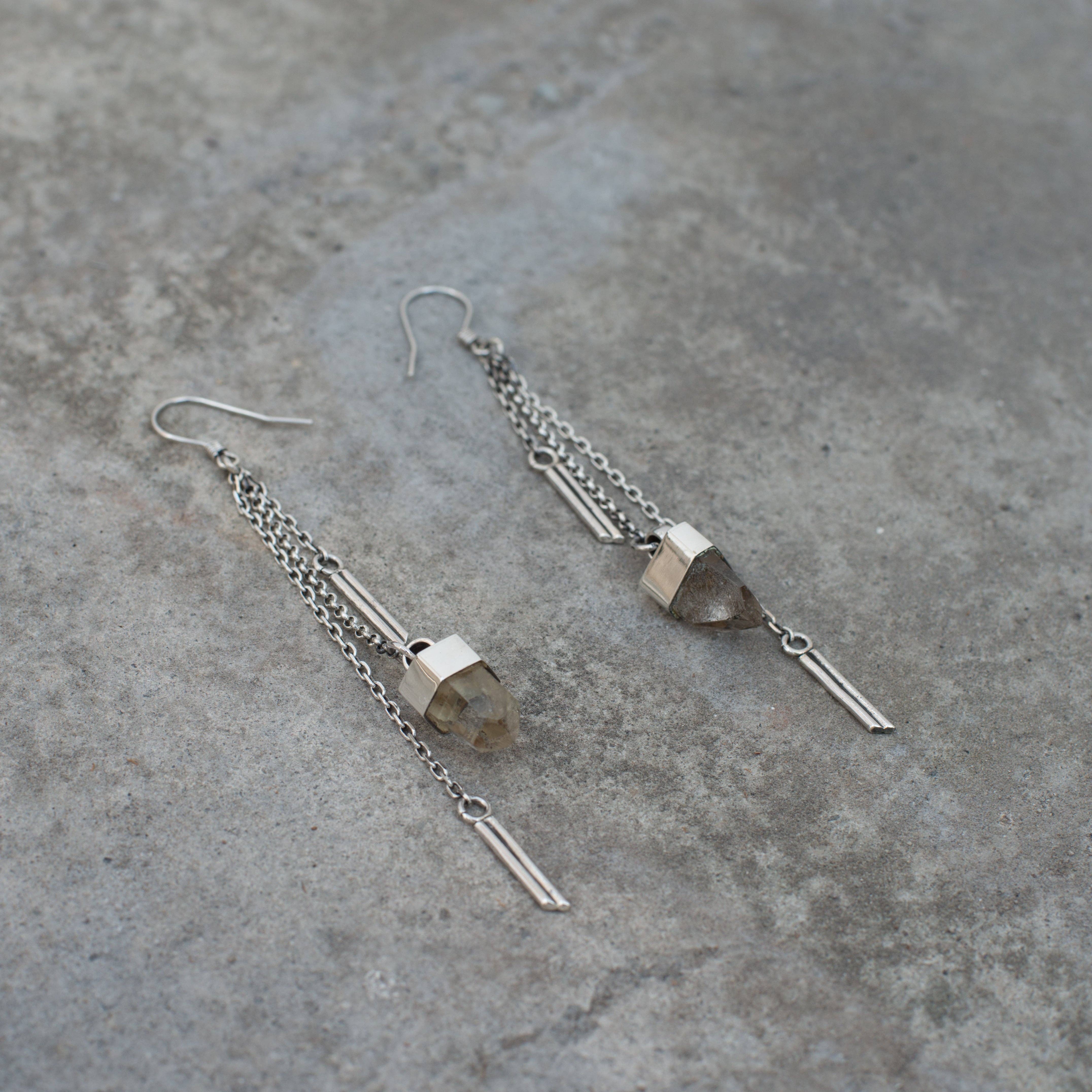 Jan Hilmer + Sparrow Crystal dangle earrings - sterling silver, featuring geometric shapes and translucent quartz crystal accents, displayed on a textured gray surface.