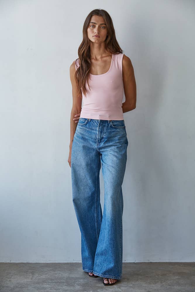 Woman wearing a light pink Double Layered Seamless Top paired with wide-leg blue jeans in a minimal studio setting