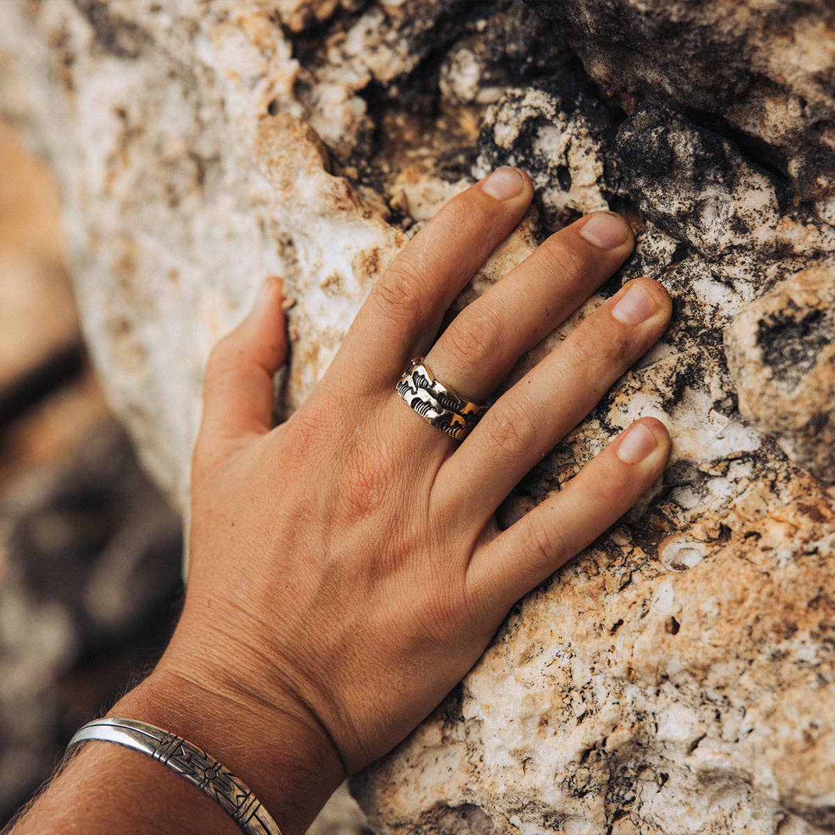 Hand wearing Medicine Wheel Cuff || Men resting on textured natural rock surface, showcasing artisan ring and bracelet.