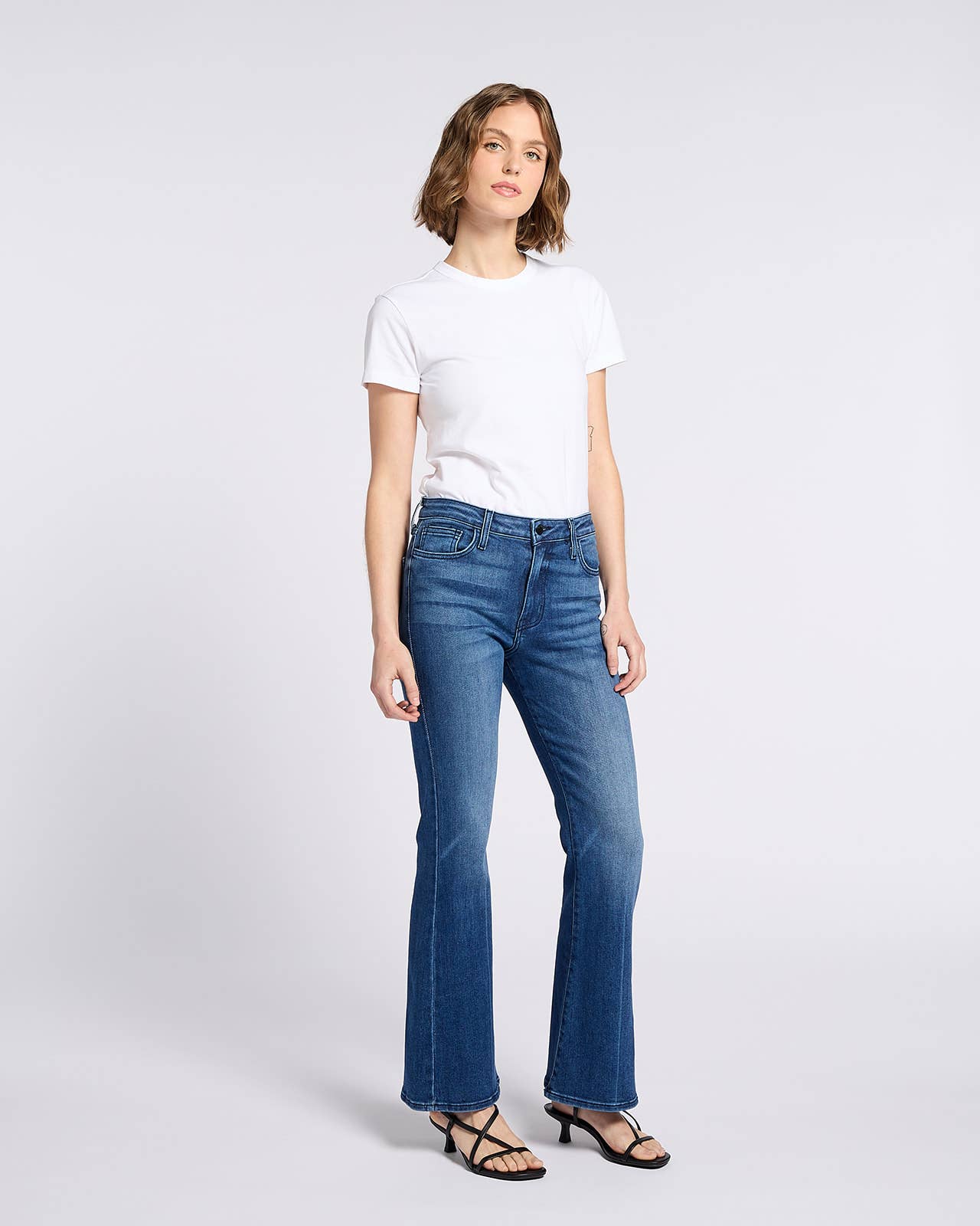 Woman wearing Bella Whisker Flare Denim jeans styled with a simple white t-shirt and black strappy sandals