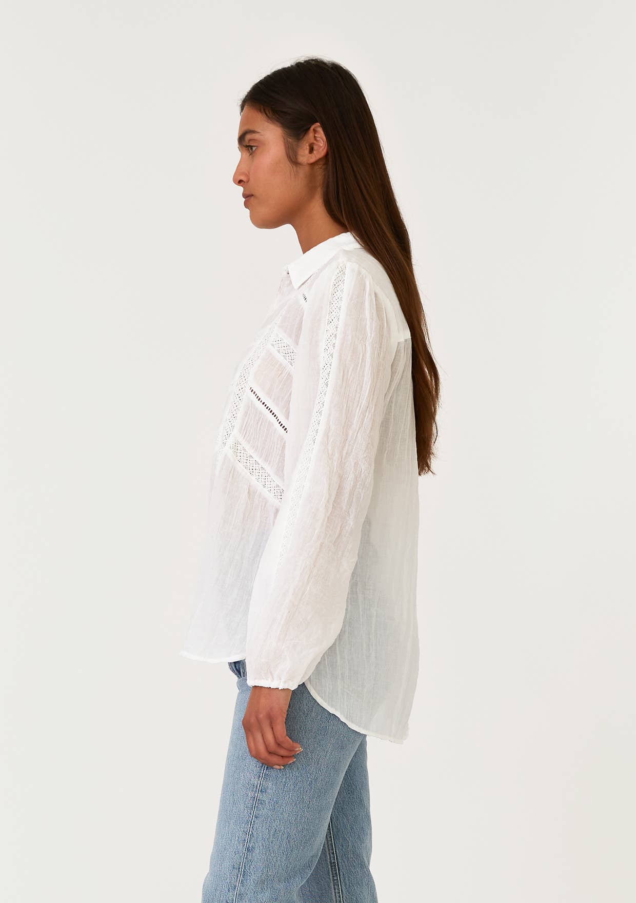 Woman wearing a white Crinkled Lace Long Sleeve Button Down Blouse with lace details, paired with blue denim jeans, side view.