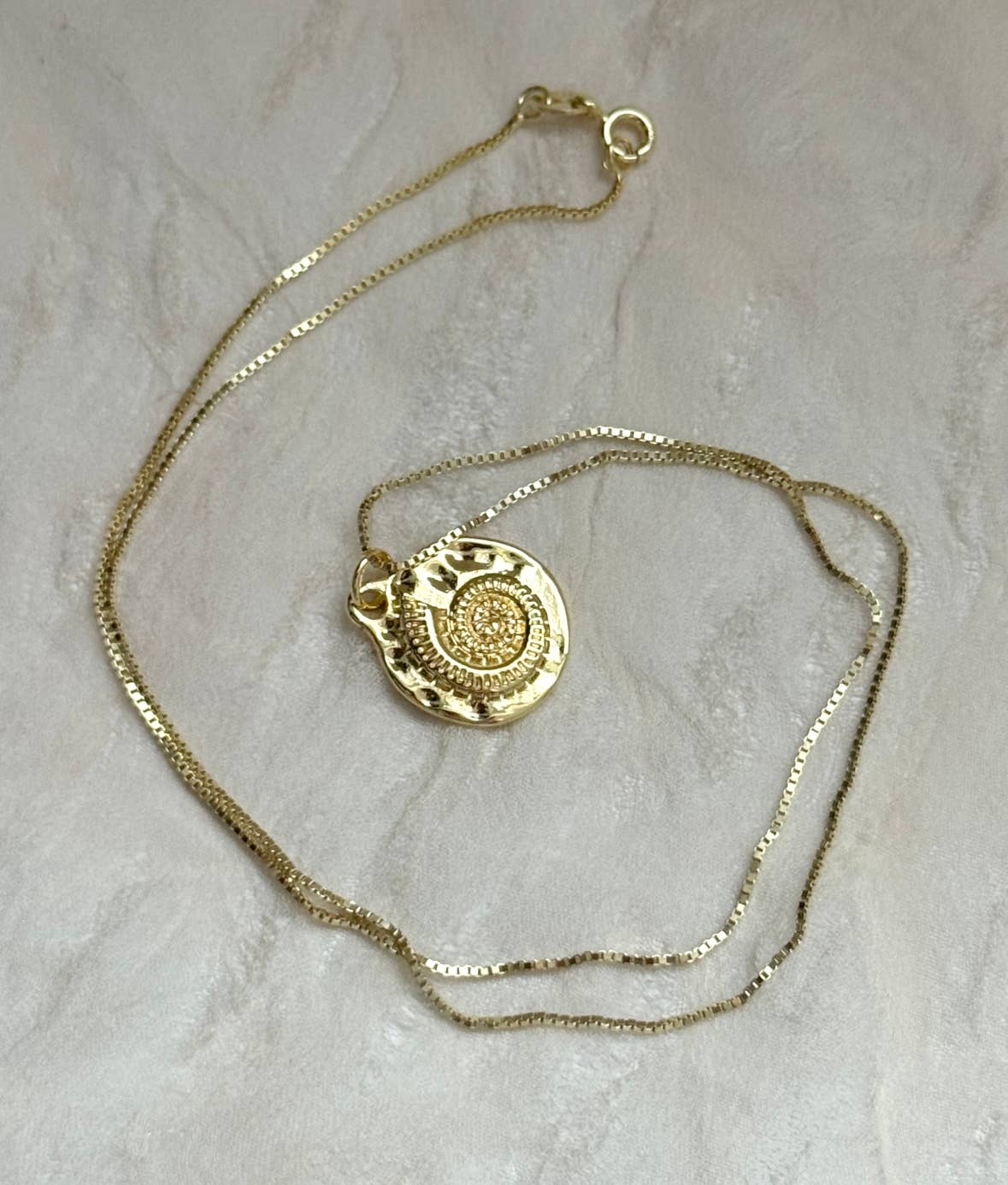 The Mar Medallion Necklace by Tramps+Thieves features a gold vermeil round shell pendant with an intricate spiral design, shown on a light, textured surface.
