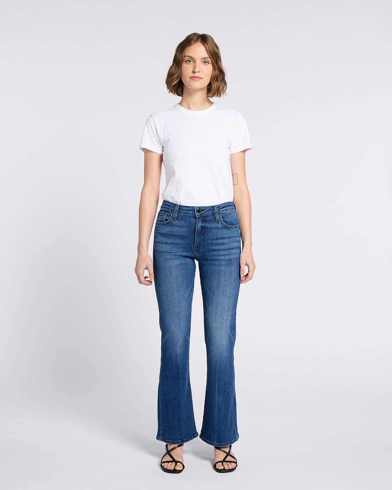Woman wearing Bella Whisker Flare Denim jeans styled with a simple white t-shirt and black sandals against a white background