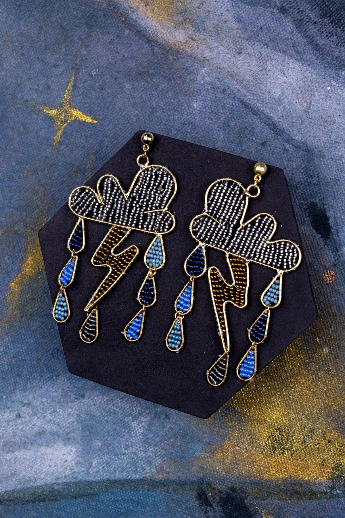 Storms a Brewin Danglers featuring blue and gold lightning bolt earrings with cloud designs on black backing