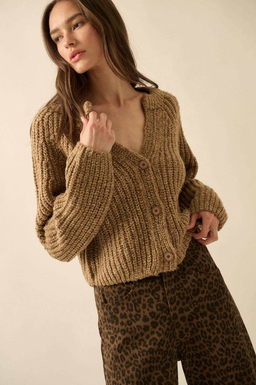 A woman in the Promesa USA Confetti Button-Front Cardigan Sweater and high-waisted leopard print pants poses against a plain beige background.