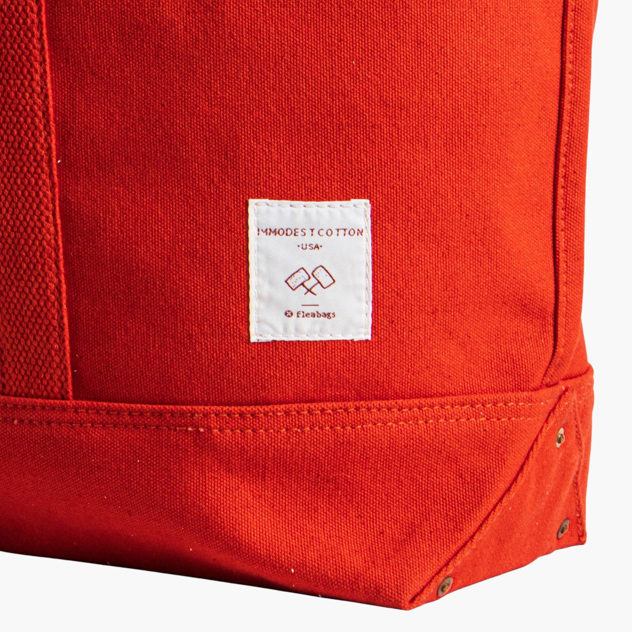 Close-up of persimmon canvas bottom corner with tag on Large East West Tote | Persimmon