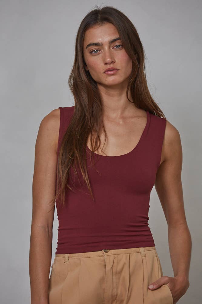 A woman with long brown hair models the By Together Double Layered Seamless Top in maroon, paired with beige pants, standing against a plain gray background and looking directly at the camera with a neutral expression.