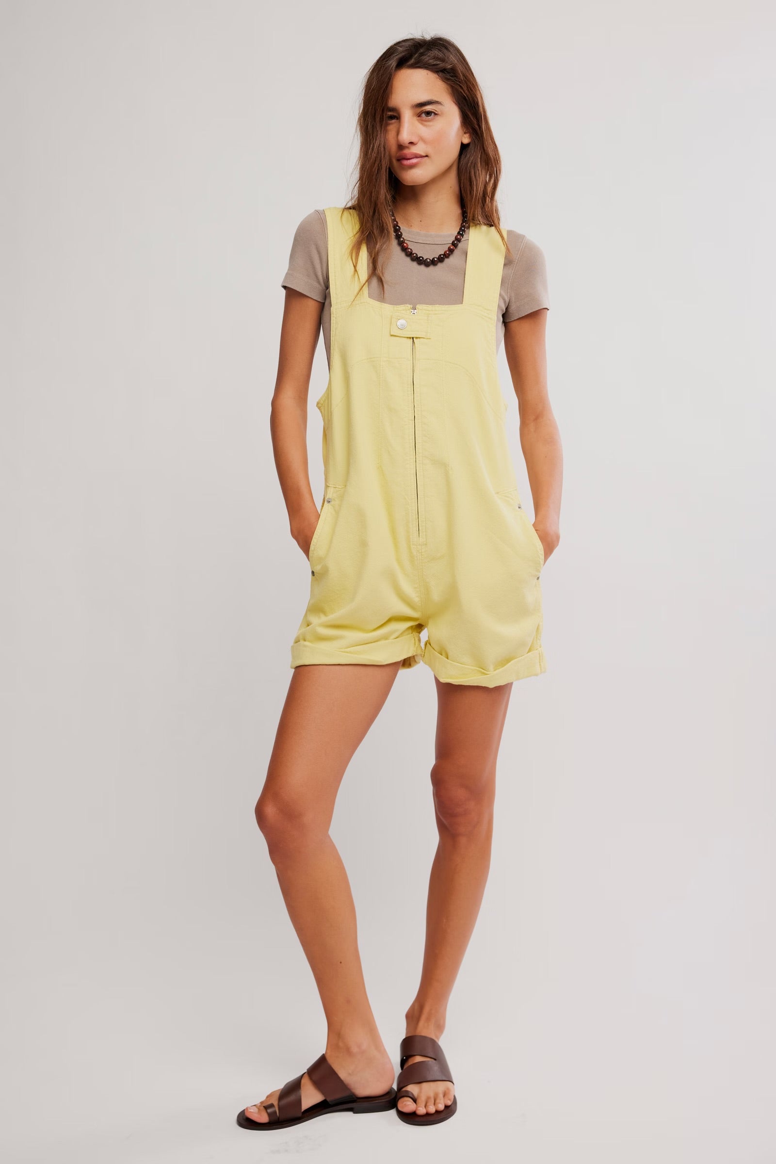 Woman wearing Free People Jude Shortall Overall Short in pale yellow with rolled hems and a beige short sleeve top
