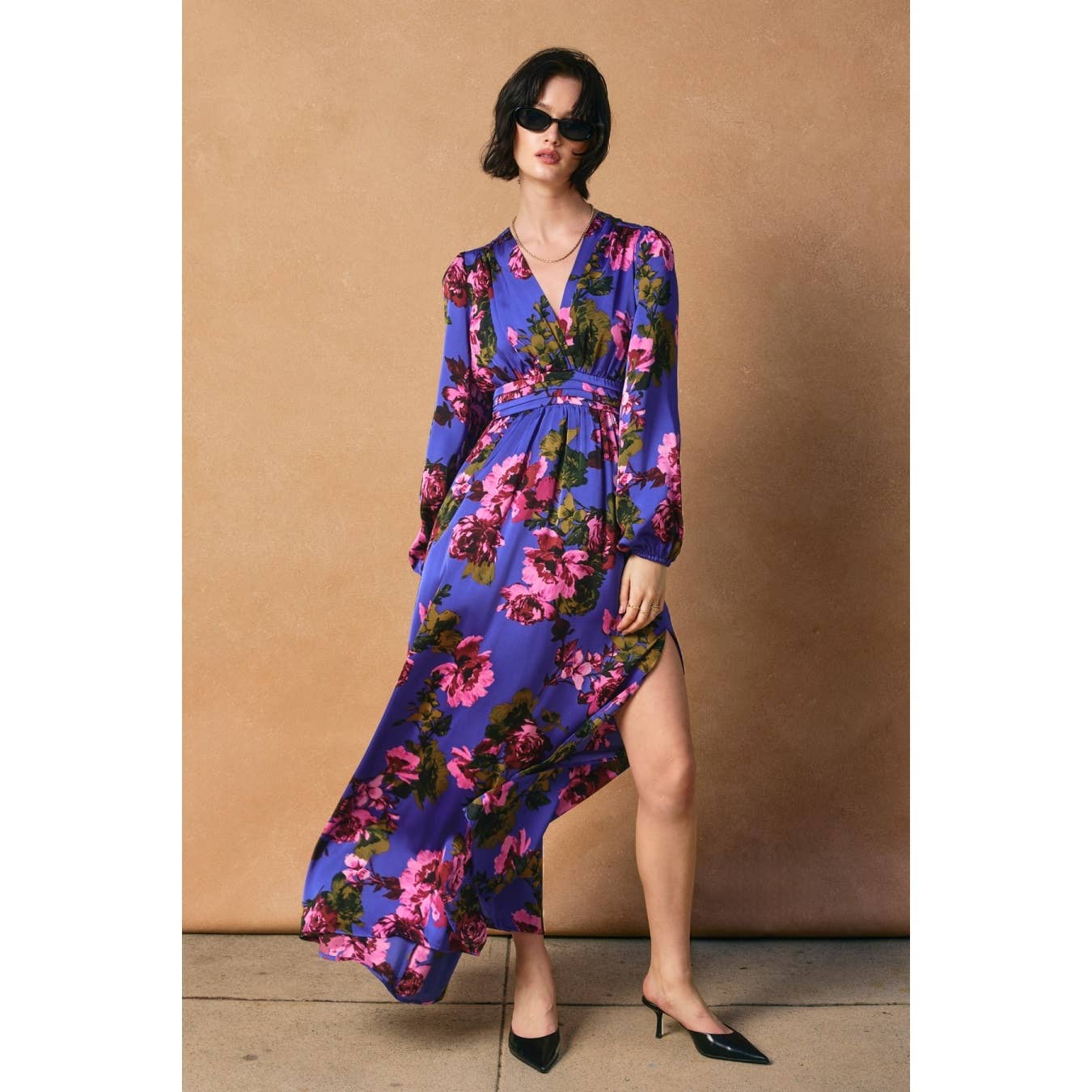 A person in the Dress Forum Mesmerizing Essence Pleated Waist Maxi Dress poses against a beige background, showcasing the side slit. They wear sunglasses and black pointed heels, with one leg slightly forward.