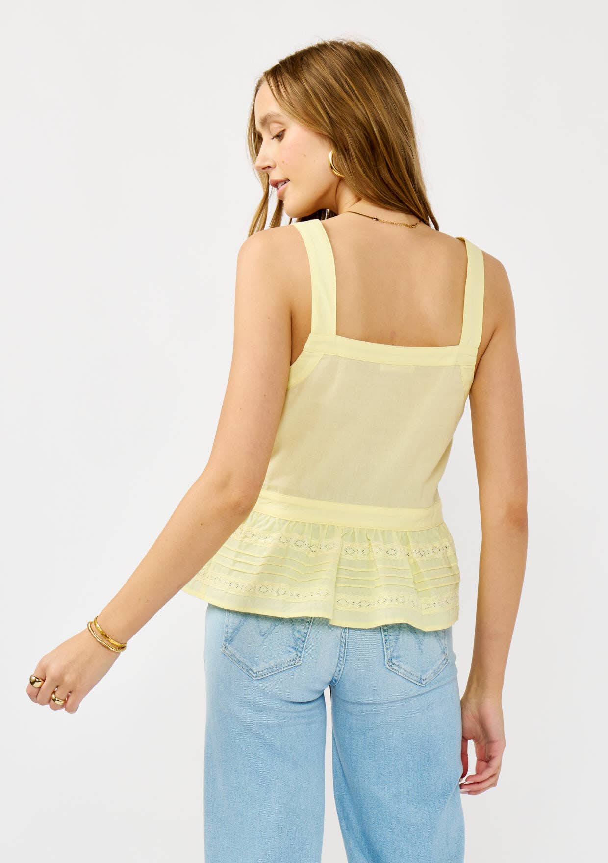 Woman wearing a pale yellow Smocked Ruffle Lace Peplum Top paired with light blue denim jeans, shown from the back