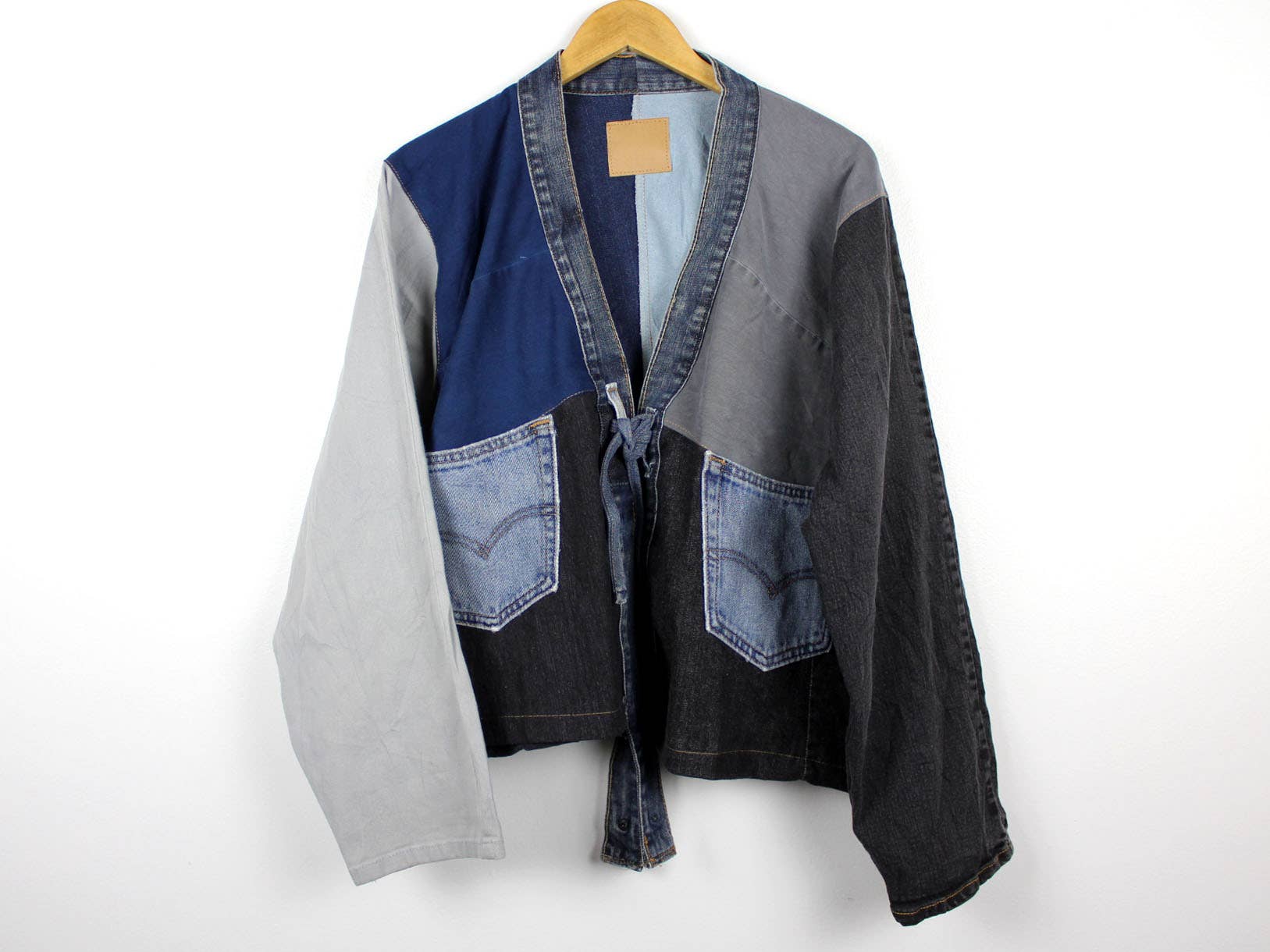 Upcycled Patchwork Denim Jacket in mixed blue and gray denim with front patch pockets and tie closure on hanger