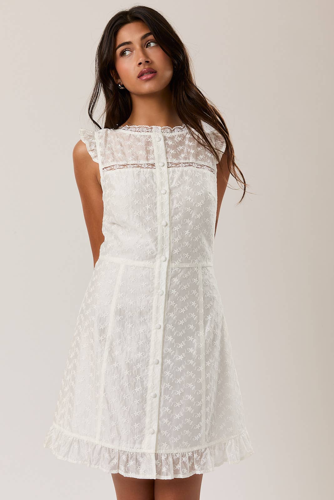 Woman wearing a white Eyelet Lace Mini Dress with sheer shoulders and front button details in a relaxed pose