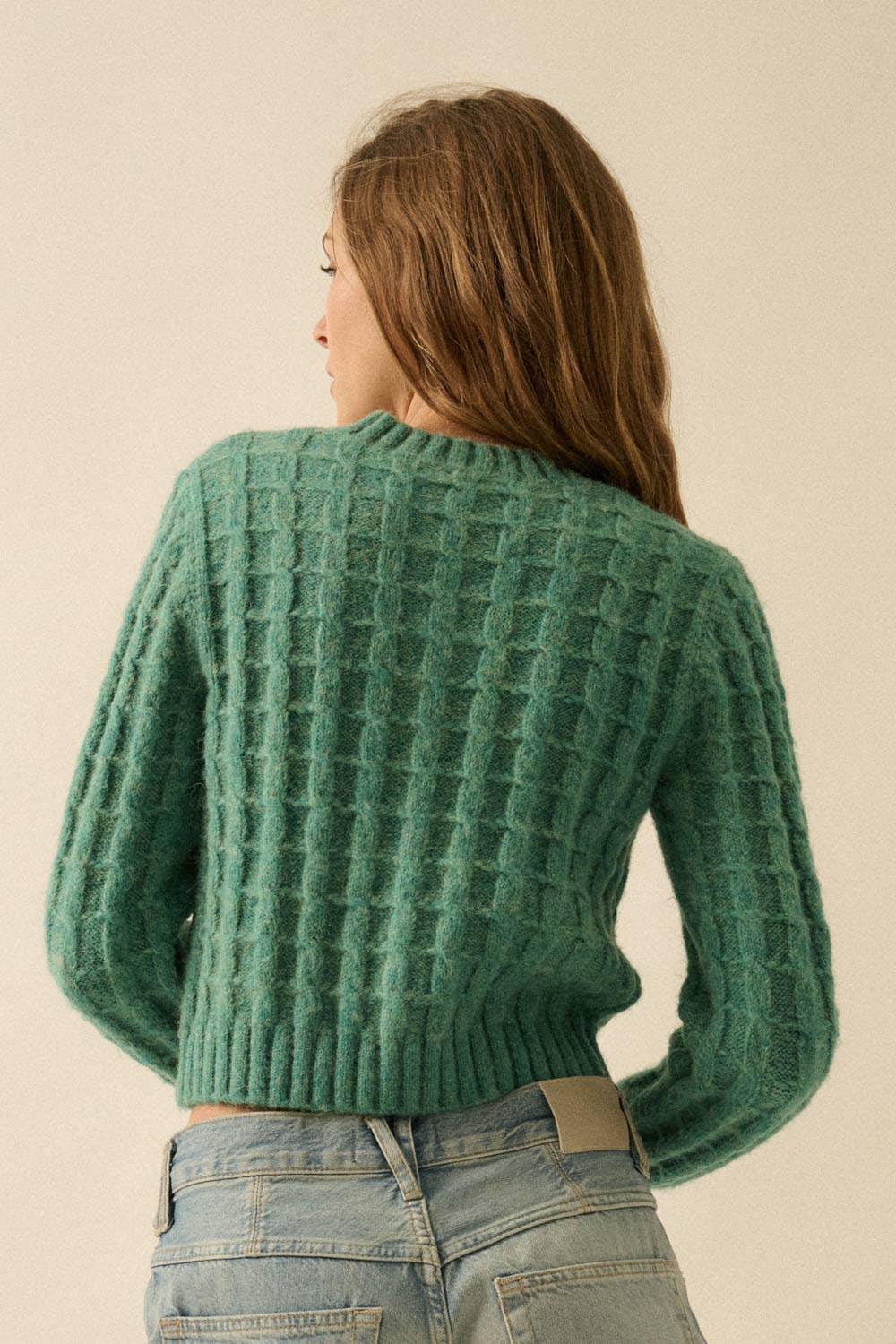 A person with long light brown hair is seen from behind, wearing the Promesa USA Cable Knit Button-Up Cardigan Sweater in green with light blue jeans against a neutral background.