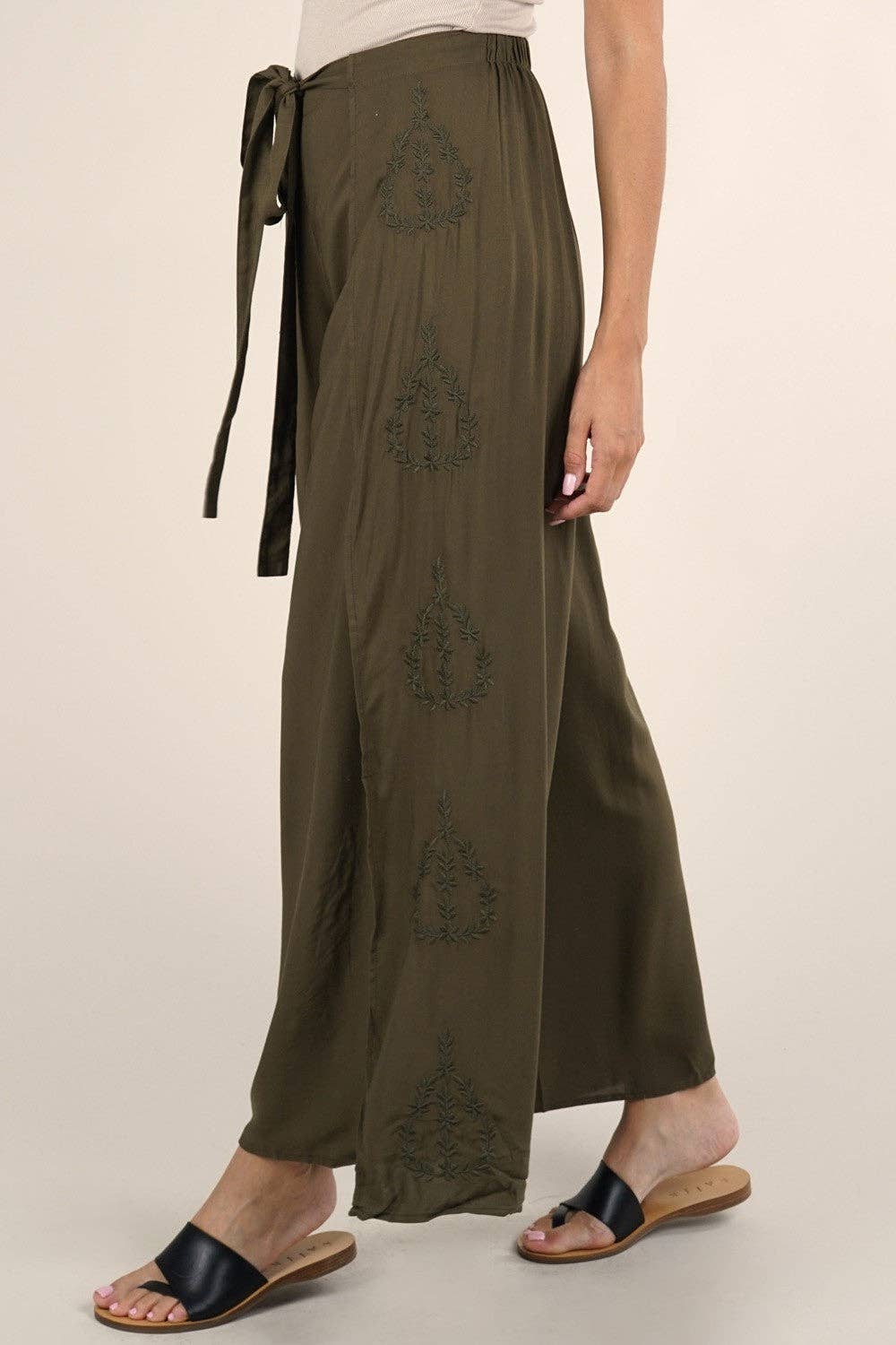 Side view of olive Boho Beach Light Weight Wrap Pant with embroidered details and a tied waist, styled with black slide sandals.