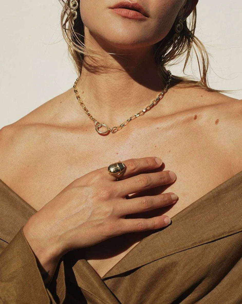 Woman wearing a gold Scarab Ring and matching chain necklace with a brown off-shoulder top in natural light