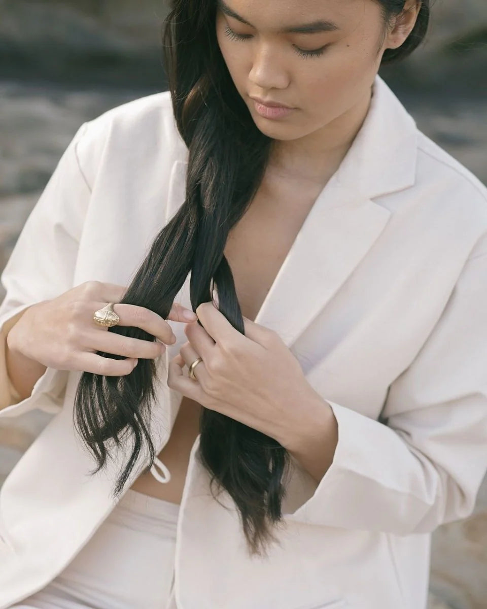 Woman in white blazer wearing a gold Scarab Ring on her finger while twisting her long dark hair outdoors