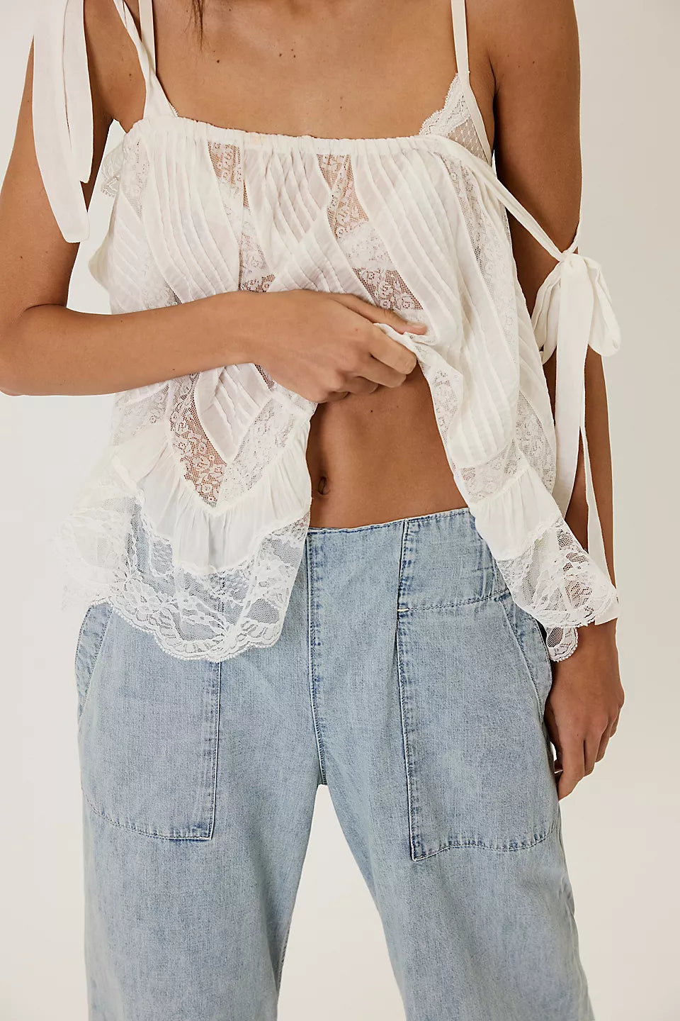 Close-up of light washed denim jeans with a relaxed fit styled with a delicate white lace and pleated top, We The Free Breezy Denim Pull-On Jeans