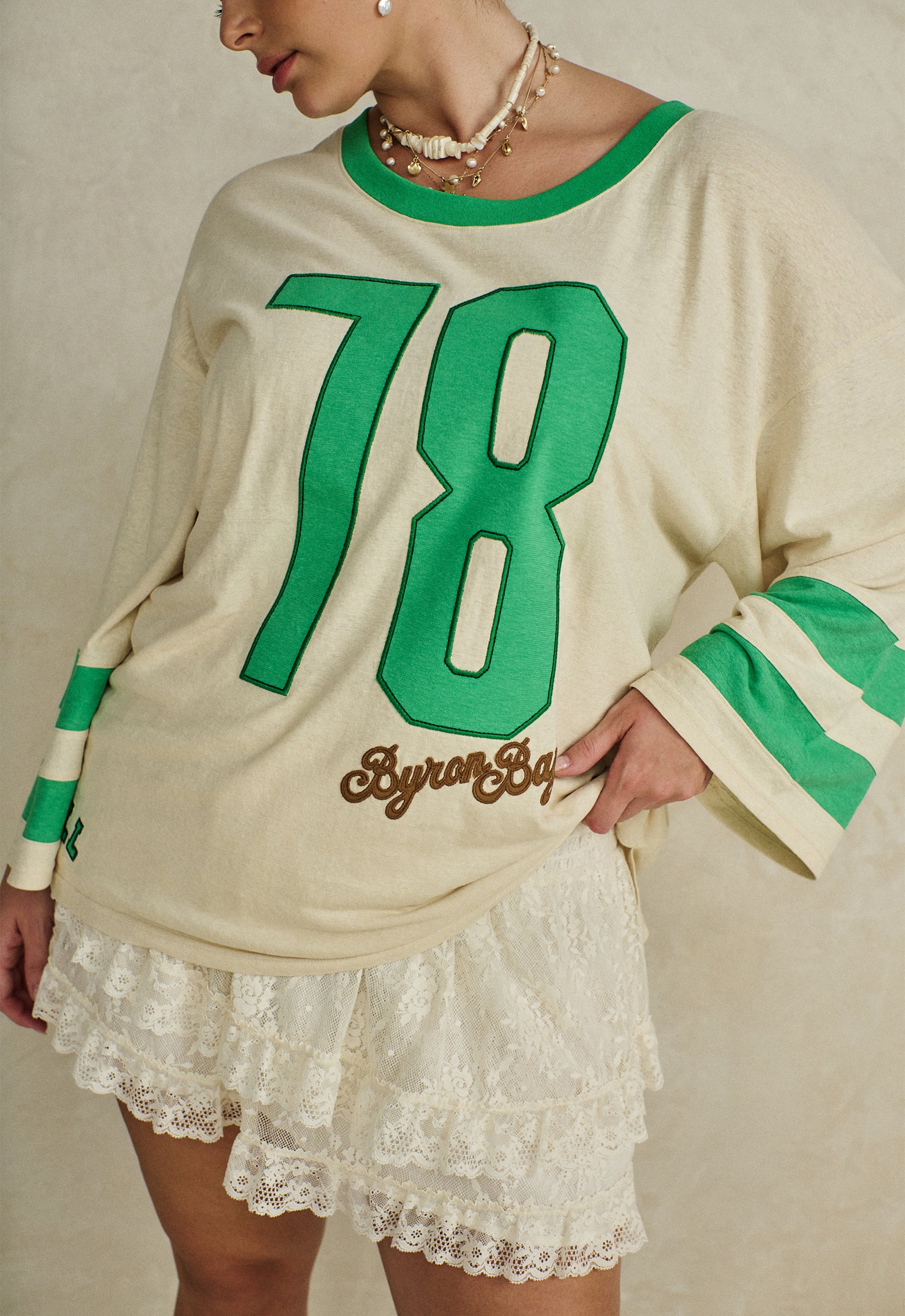 Woman wearing a Homecoming Long Sleeve Biker Tee with green number 78 and striped sleeves paired with lace shorts