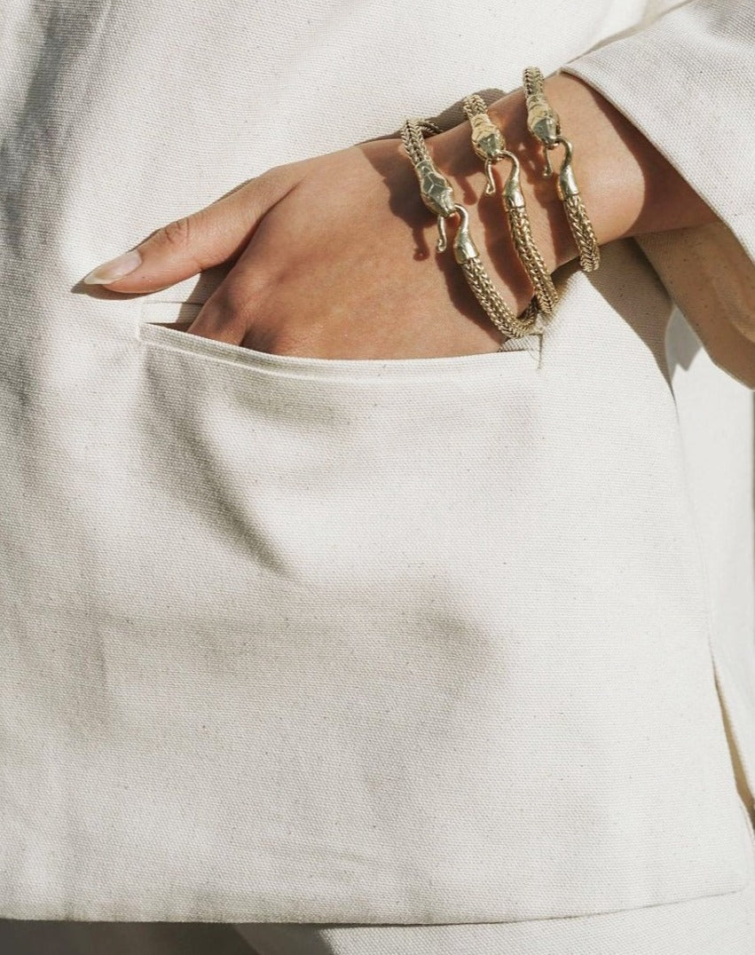 Close-up of a hand in a beige pocket wearing three textured gold Serpent Bracelet pieces with clasp detail.