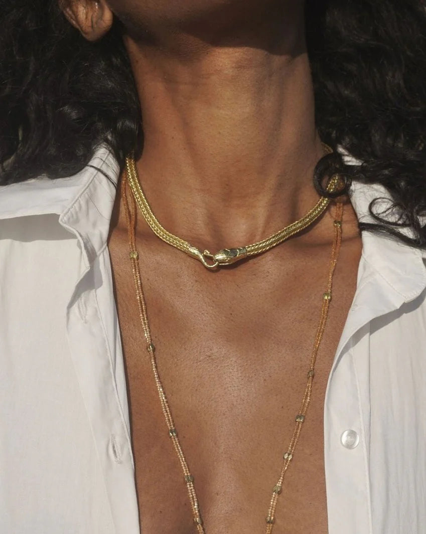 Close-up of a golden Serpent Choker Necklace worn with layered delicate chains and an open white shirt collar.