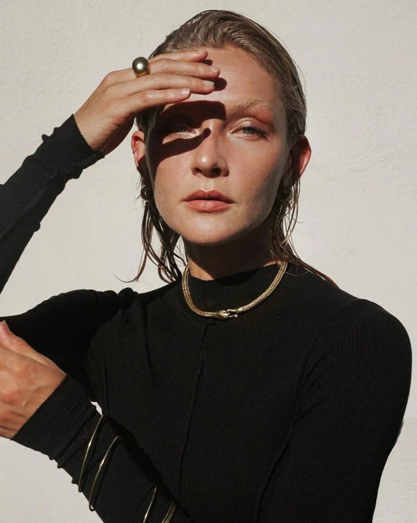 Woman wearing a gold Serpent Choker Necklace with a black top, posing with hand shading her eyes in natural light