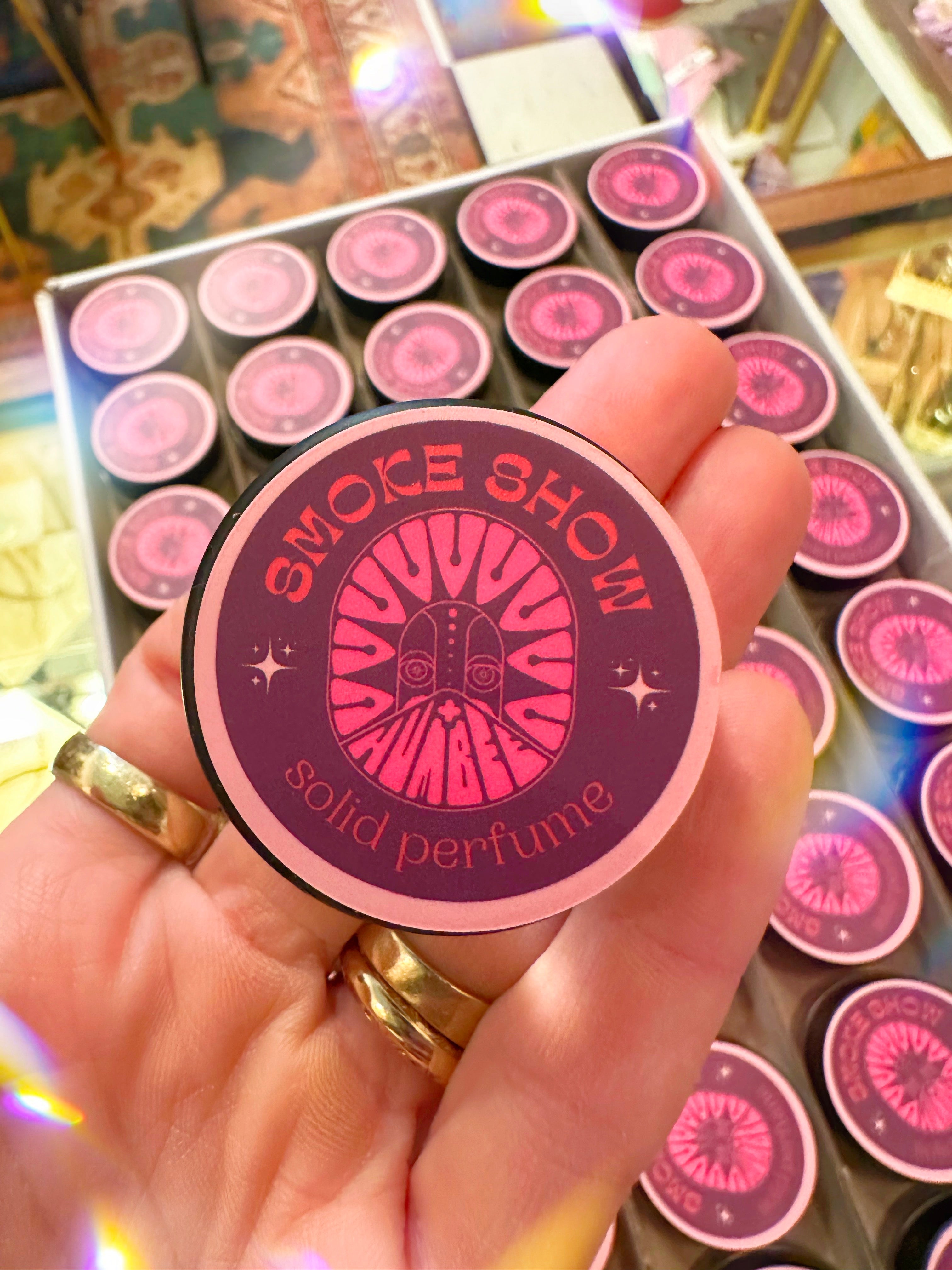 Solid perfume container with 'Smoke Show' branding held by a hand.