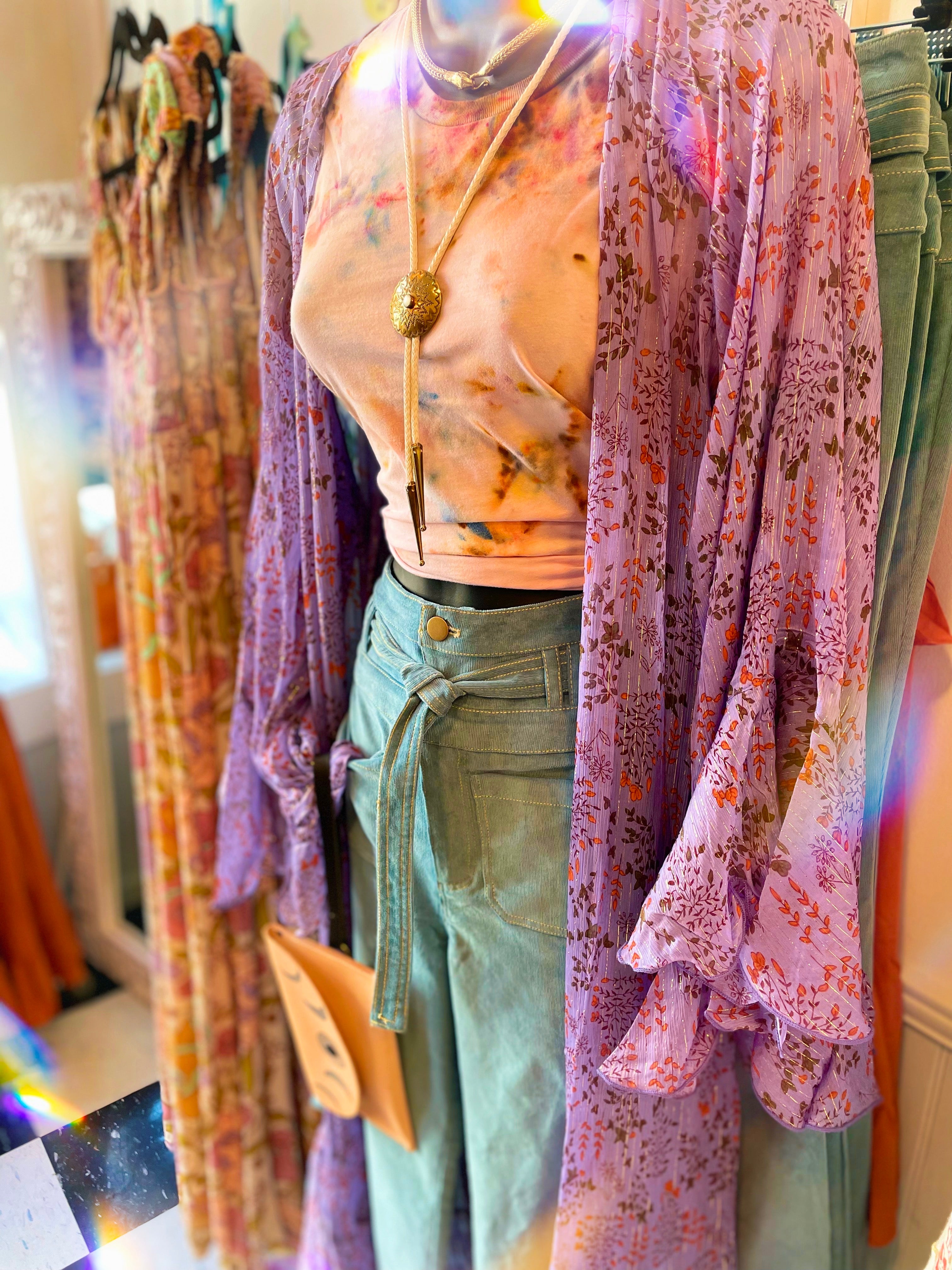 Mannequin wearing a floral top and light blue pants with colorful clothing in the background.