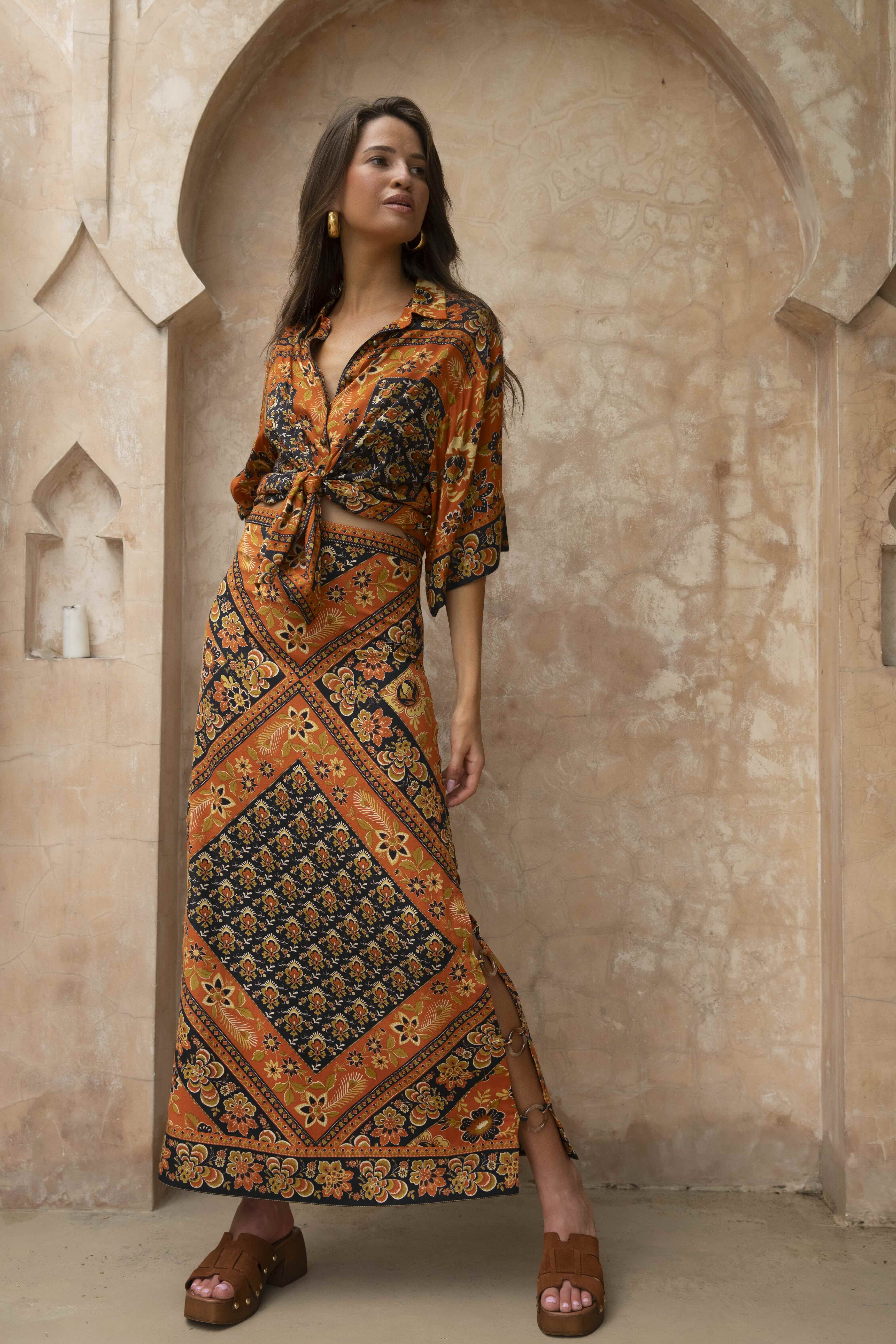 Woman wearing Lois Shirt - Saffron with vibrant orange and black bohemian patterns in an ornate archway setting