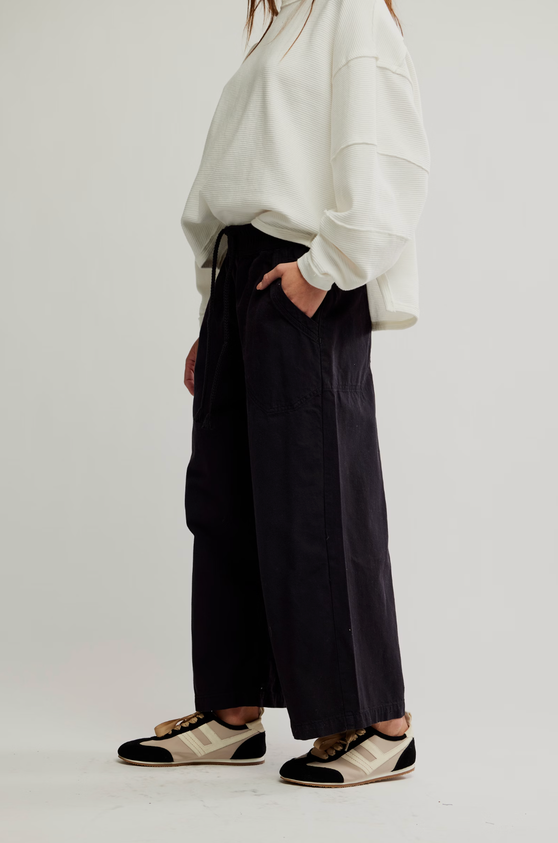 Side view of a woman wearing We The Free Easy Peasy Pull-On Jeans with a loose white top and black sneakers.
