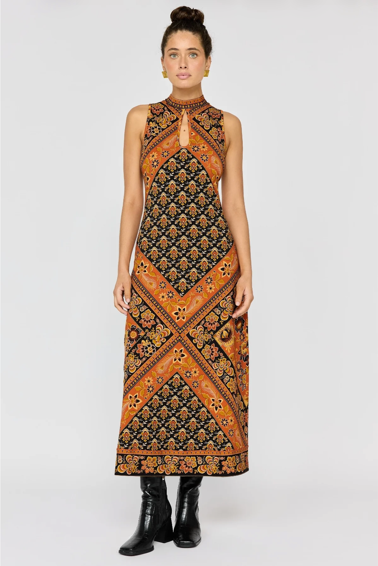 Woman wearing a patterned sleeveless high-neck Sydney Midi Dress in Saffron paired with black boots.
