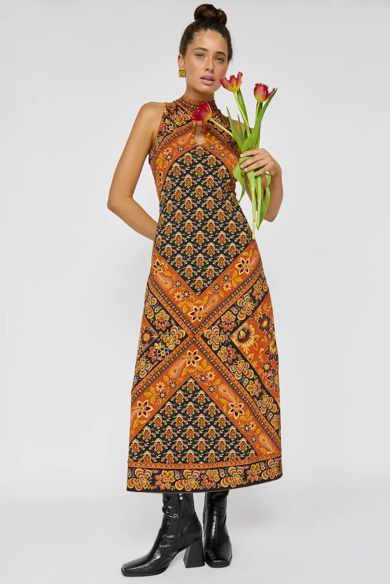 Woman wearing a patterned Sydney Midi Dress in Saffron holding red tulips paired with black ankle boots.