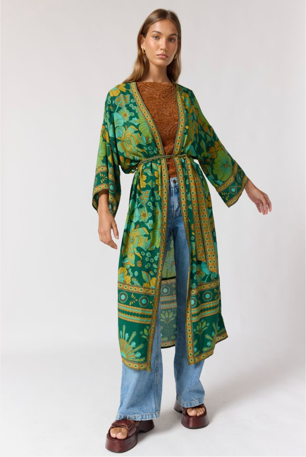 Woman wearing Jade Robe in Emerald with floral and geometric patterns over brown top and wide-leg jeans, styled confidently.