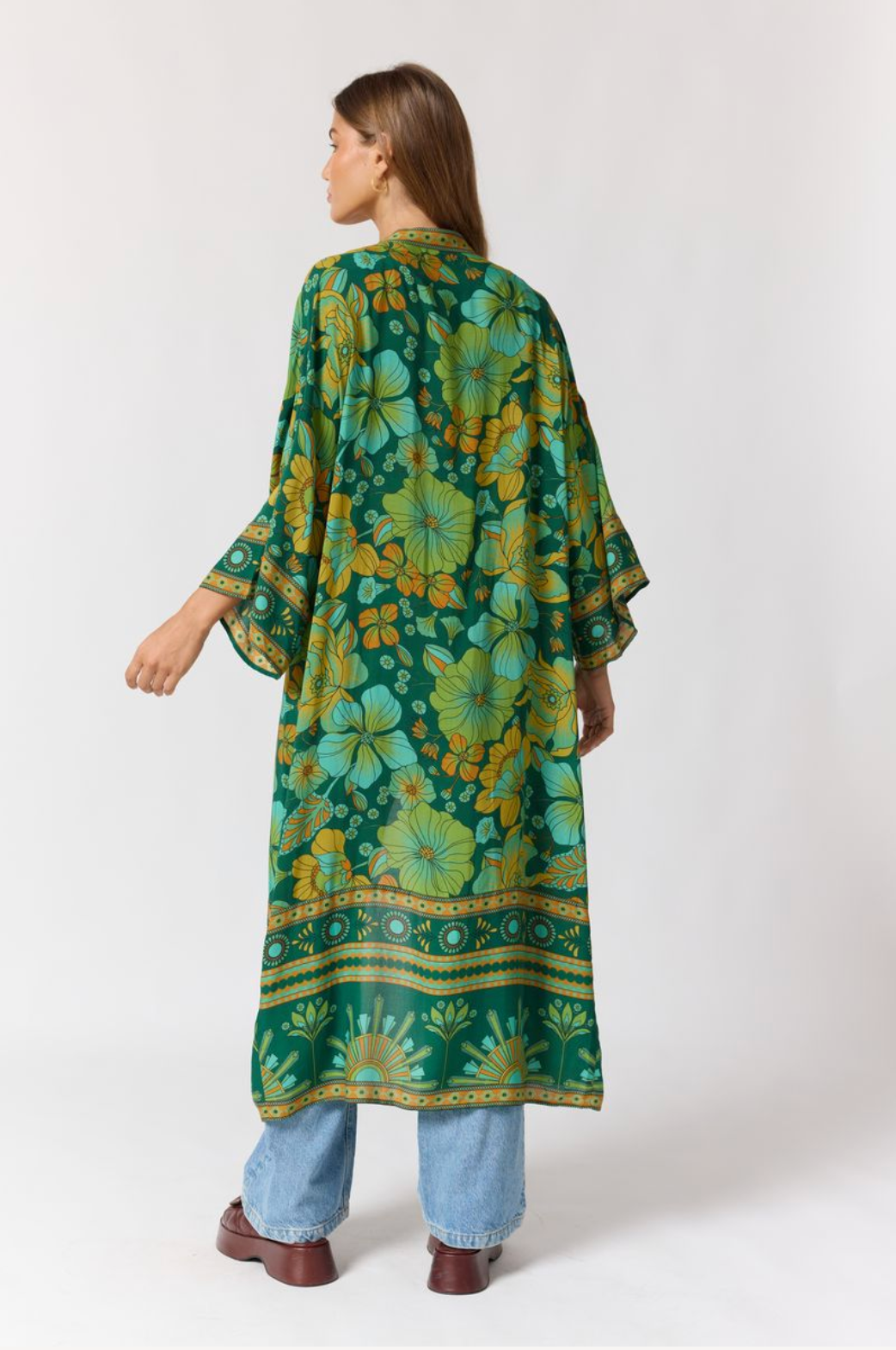 Woman wearing a flowing Jade Robe in Emerald with vibrant floral patterns and wide sleeves over jeans and boots.