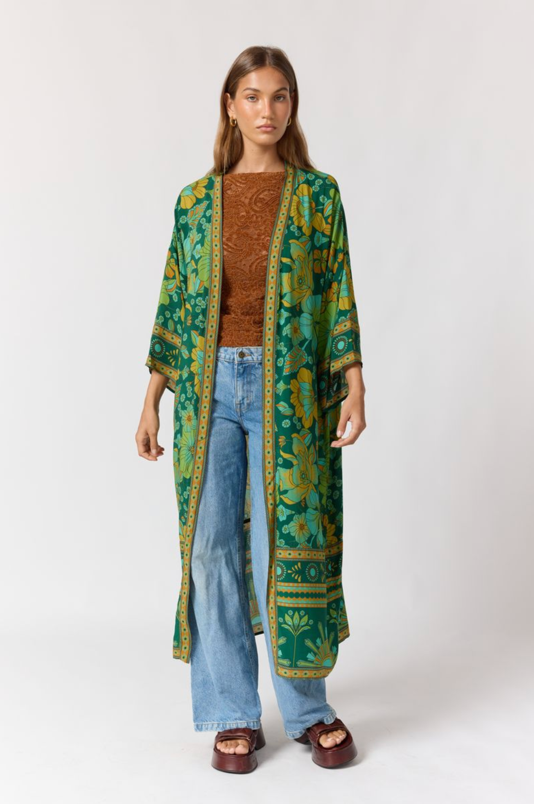 Woman wearing Jade Robe in Emerald with floral patterns over brown top and light blue jeans in minimalist studio setting.