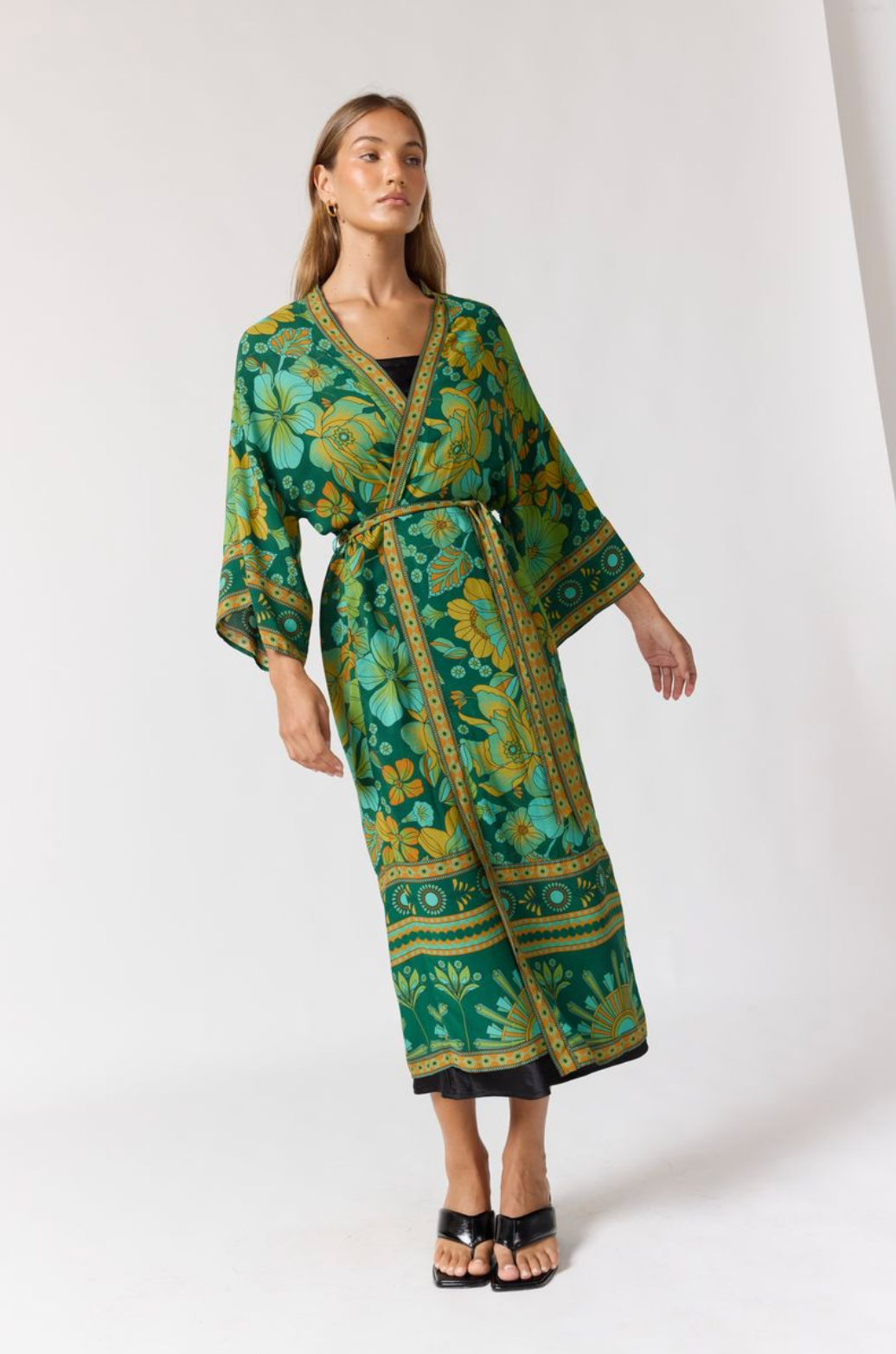 Woman wearing flowing floral patterned Jade Robe in Emerald with wide sleeves and belt standing against white background