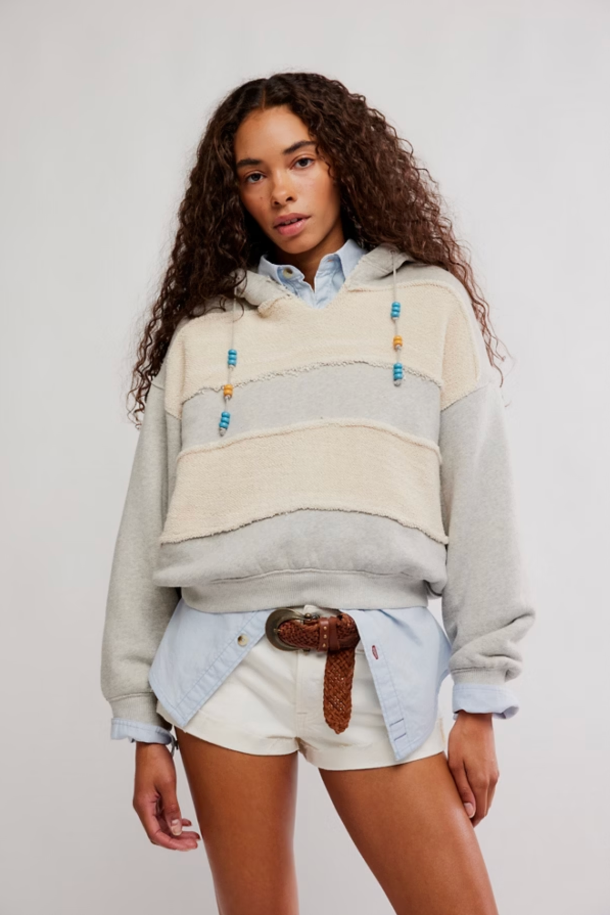 Woman wearing a cozy striped Camp Crush Hoodie with bead details layered over a light blue shirt and white shorts.