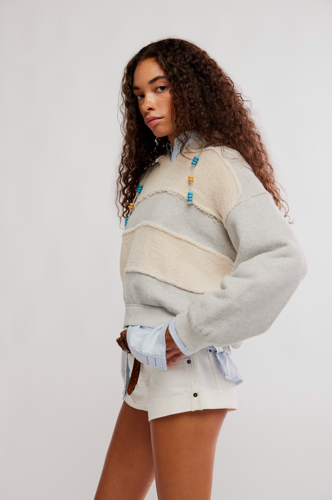 Woman wearing a layered light gray and beige Camp Crush Hoodie paired with white shorts and beaded necklace