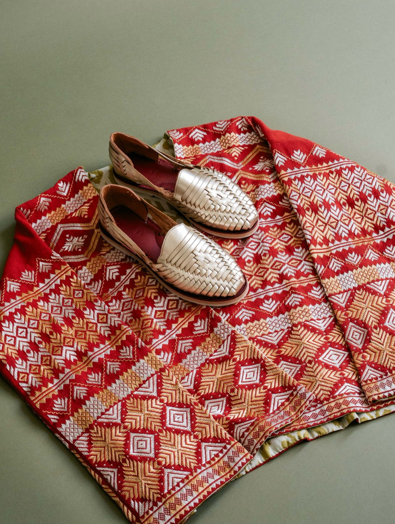 Gold Slip On Huarache Sandal placed on red and beige patterned textile with artisan design details.